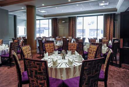 A room with large windows, round tables seating 8, and high backed chairs with velvery purple seats