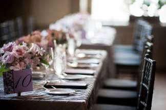 Rectangular tables set with centerpiece bouquets of pink roses, light coming through the window with the background in soft focus